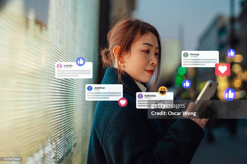 Young Asian business woman connecting to social media platforms with smart phone against led lights on city street