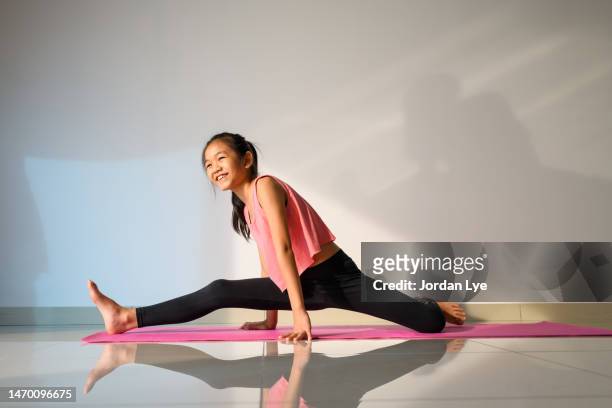 young woman practicing yoga at home, doing split on an exercise mat. - gymnastic asian stockfoto's en -beelden