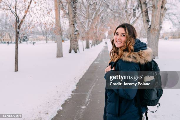 cheerful university student standing looking over her shoulder at camera on campus on a snowy day in colorado - colorado state university stock pictures, royalty-free photos & images