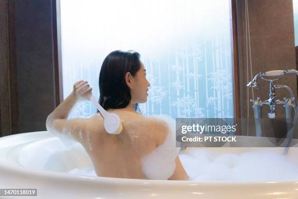 a woman is scrubbing herself in the bathtub. - woman shower candle stock-fotos und bilder