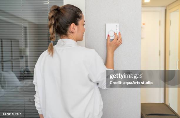 la donna che regola la temperatura ambiente dal pannello dell'aria condizionata - riscaldamento domestico foto e immagini stock
