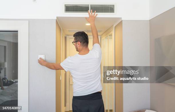 the man who adjusts the room temperature from the air conditioning panel - air conditioner interior wall stock pictures, royalty-free photos & images