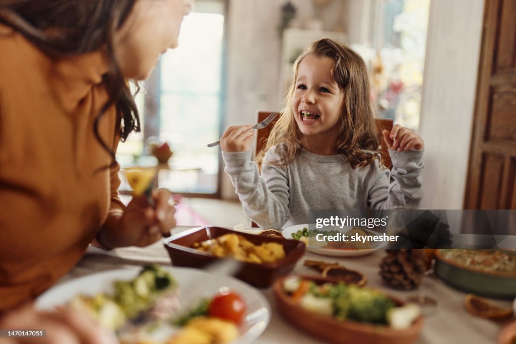 Ragazza felice che parla con sua madre durante un pasto al tavolo da pranzo.