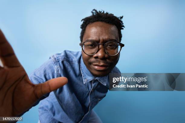 studio shot of serious black man in jeans against blue background. - hand wide angle stock pictures, royalty-free photos & images