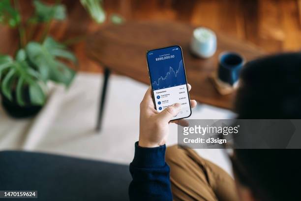 over the shoulder view of young asian man managing personal banking and finance with online banking app on smartphone at home. financial planning. investment. wealth management, banking and finance concept. smart banking with technology - bank statement bildbanksfoton och bilder