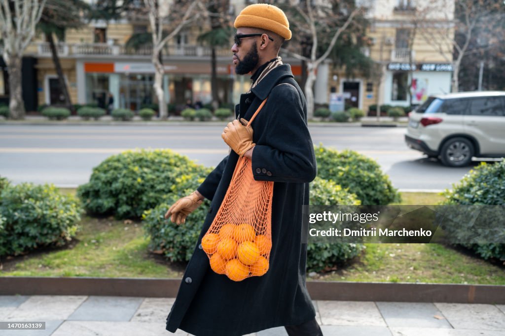 African American walking city street carrying oranges in reusable cotton mesh shopping bag