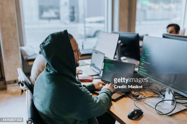 young male hacker using laptop while coding on computer at desk in startup company - selective focus imagens e fotografias de stock