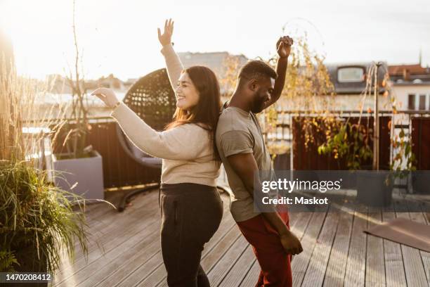 side view of carefree couple dancing while standing back to back at terrace - dancing back to back stock pictures, royalty-free photos & images
