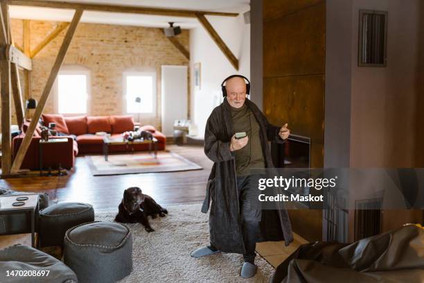 carefree senior man dancing and listening to music while standing on carpet at home - dog listening stock pictures, royalty-free photos & images