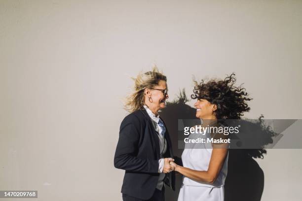happy mature lesbian couple holding hands while standing against wall - arabic wedding stock pictures, royalty-free photos & images