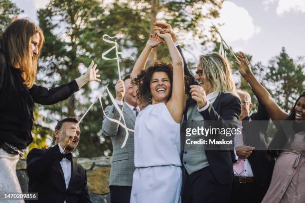 happy lesbian couple holding hands dancing amidst family and friends during wedding celebration - arabic wedding stock pictures, royalty-free photos & images