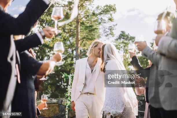 affectionate bride and groom kissing on mouth amidst guests raising toasts at wedding ceremony - arabic wedding stock pictures, royalty-free photos & images