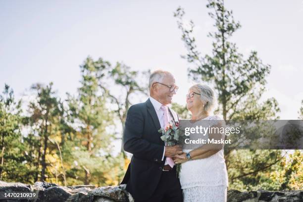 smiling senior couple looking at each other while holding bouquet at wedding - old couple wedding stock pictures, royalty-free photos & images