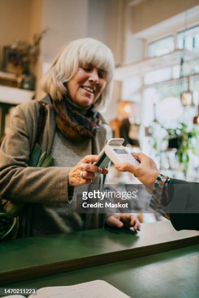 senior woman paying via tap to pay method while doing shopping at store - apple pay imagens e fotografias de stock