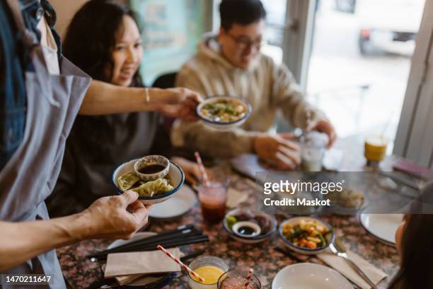male waiter serving dumplings to friends at restaurant - chinese restaurant stock pictures, royalty-free photos & images