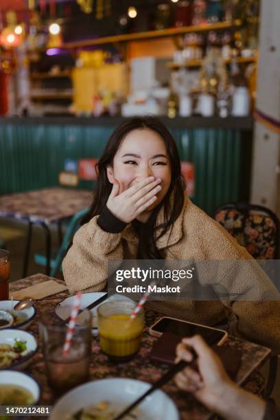 woman laughing while covering mouth at restaurant - 21 & over stock pictures, royalty-free photos & images