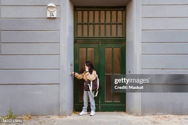 woman talking on smart phone while doing intercom standing at apartment entrance - ringing doorbell - fotografias e filmes do acervo