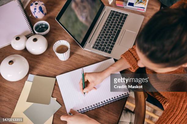 high angle view of female freelancer preparing to-do list in spiral book while sitting with laptop at home - dining table icon stock pictures, royalty-free photos & images