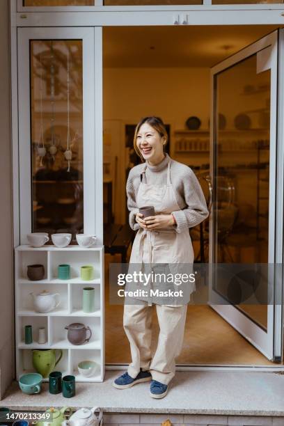 young female potter laughing while standing at workshop doorway - pottery stock pictures, royalty-free photos & images