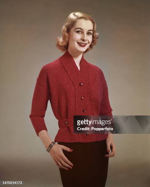 Posed studio portrait of a woman wearing a red knitted jacket in flecked wool, fitted at the waist with matching tabs, London, 4th January 1958.