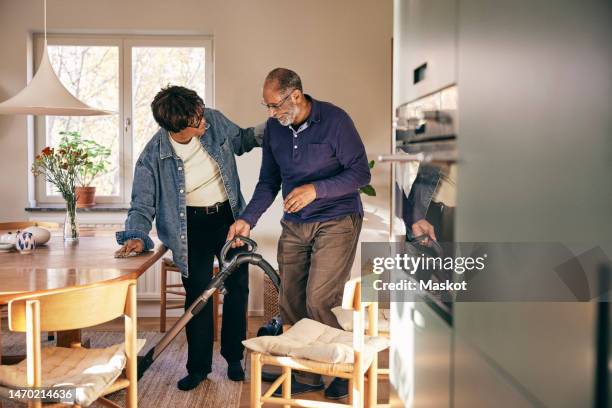 senior woman talking to man cleaning home with vacuum cleaner - poetshulp stockfoto's en -beelden