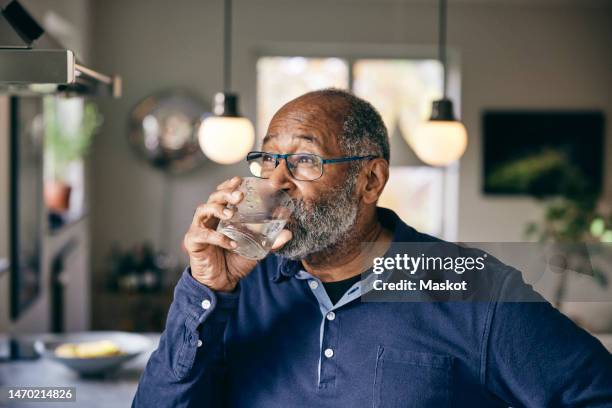 contemplative senior man drinking water at home - agua dulce fotografías e imágenes de stock