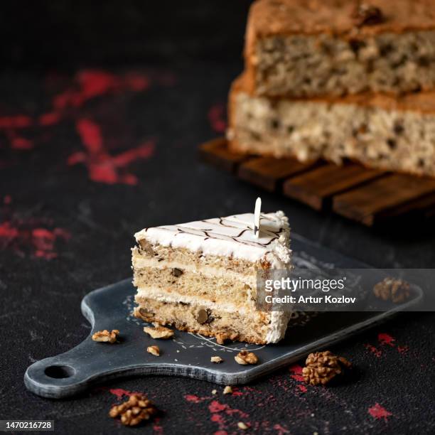 piece of festive biscuit nut cake with butter cream on black cutting board with walnuts. pie in background. homemade birthday cake. dark background. sectional side view. copy space. soft focus - butter tart stock pictures, royalty-free photos & images