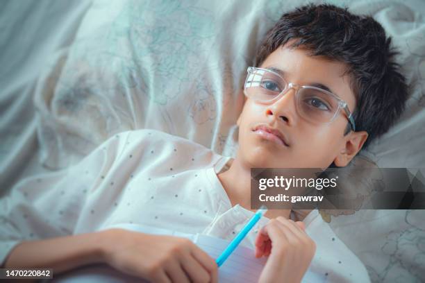 sad boy contemplates while lying on the bed with a notebook and pen. - lightskinned stock pictures, royalty-free photos & images