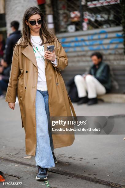 Guest wears black sunglasses from Dolce & Gabbana, gold micro earrings, a white with green inscription print pattern sweater, a brown shiny leather...