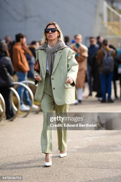 Guest wears black futurist sunglasses, a gray wool knot on the shoulder, a white t-shirt, a pale green oversized blazer jacket, matching pale green...