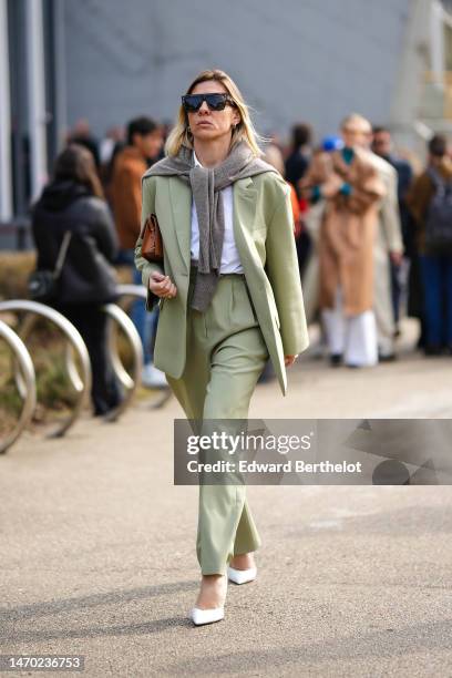 Guest wears black futurist sunglasses, a gray wool knot on the shoulder, a white t-shirt, a pale green oversized blazer jacket, matching pale green...