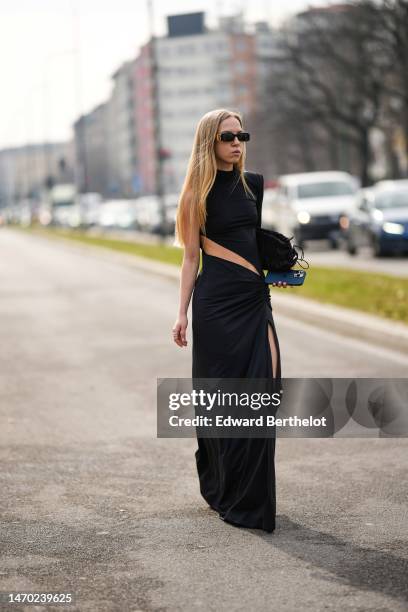 Guest wears black sunglasses from Balenciaga, silver earrings, a black turtleneck asymmetric shoulder / one long sleeves / cut-out waist long slit /...
