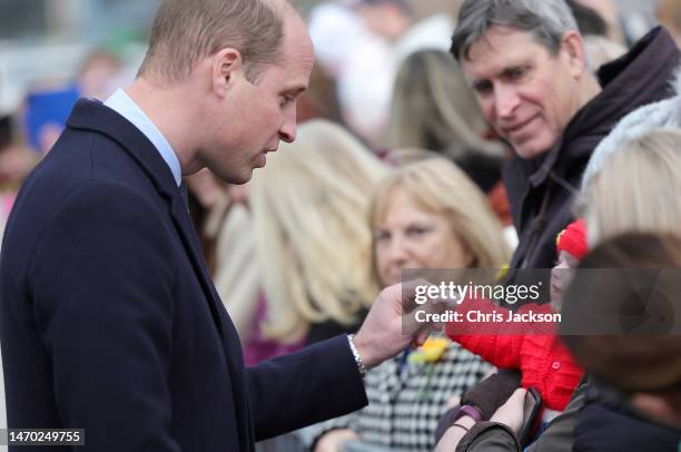 Prince William, Prince of Wales holds the hand of a young baby as he departs Aberavon Leisure & Fitness Centre with Catherine, Princess of Wales...