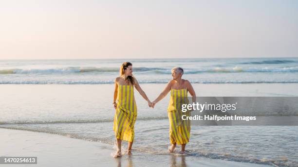 senior mother walking on the beach with her adult daughter. - matching outfits stock pictures, royalty-free photos & images