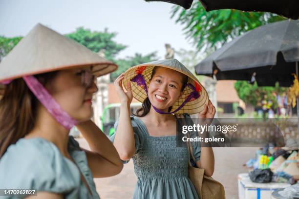 two vietnamese woman buying straw hats in village - vietnamese culture stock pictures, royalty-free photos & images