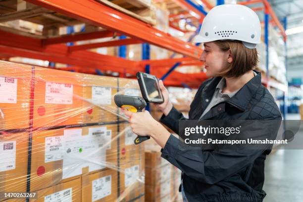 implementing rfid tags help make delivery easier and growing up your business sustainably. caucasian warehouse worker with safety helmet using a barcode reader to scan qr code on the box standing in the distribution warehouse. looking at tablet - scan barcode stock pictures, royalty-free photos & images