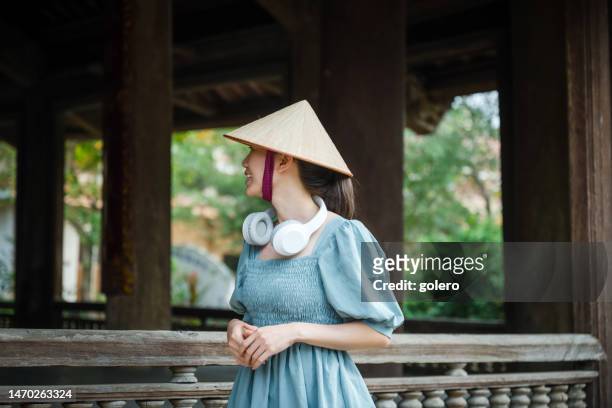 vietnamesin mit kopfhörern und strohhut im alten dorf - vietnamesische kultur stock-fotos und bilder