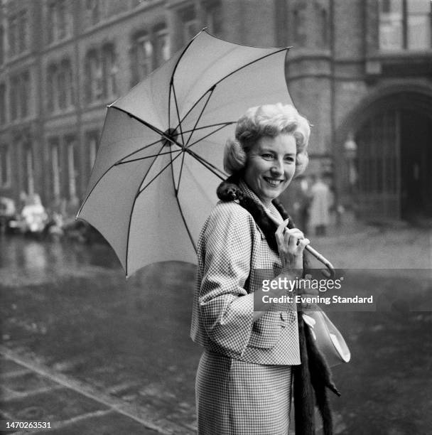 Singer Vera Lynn smiles under the cover of an umbrella outside the law courts after successfully defending a music copyright infringement case for...
