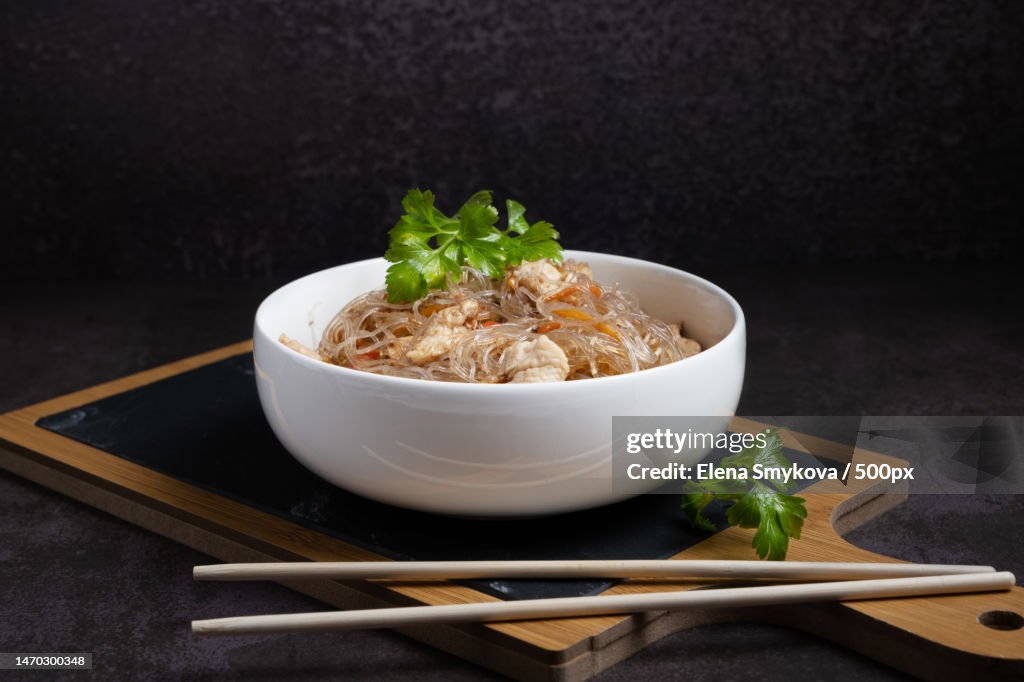 Fried funchosa with chicken in a white bowl with chopsticks on a serving board,Moscow,Russia