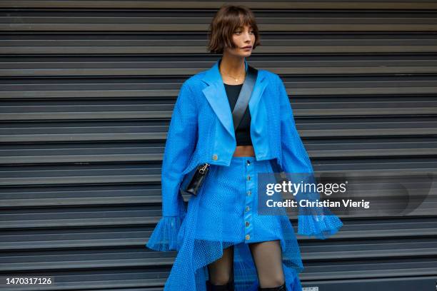 Taylor LaShae wears blue jacket with wide ruffled laced sleeves, skirt with buttons, tights, black knee high boots, black cropped top outside...