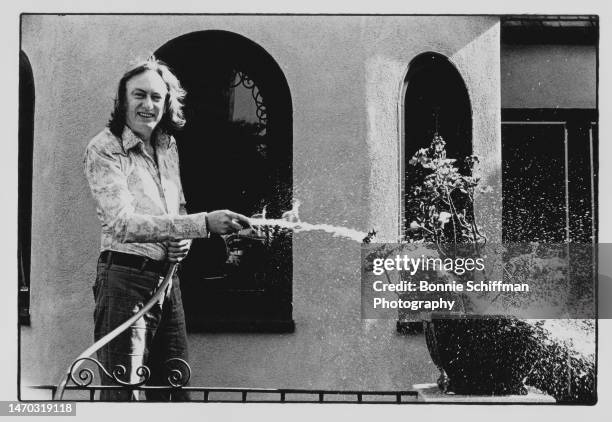 Musician and Troubadour Owner Doug Weston sprays hose on potted plant and smiles at camera in Los Angeles in 1979.
