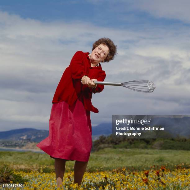 Chef Julia Child swings a large wire whisk like a baseball bat in a field of yellow flowers in Santa Barbara in 1987.