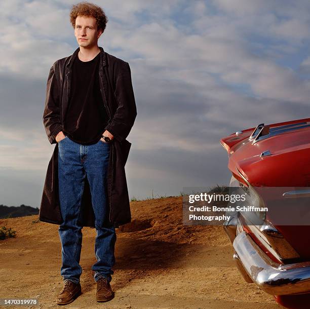Filmmaker Steven Soderbergh poses outside with a red classic car and stares at camera with hands in his jean pockets in 1989 in Los Angeles.