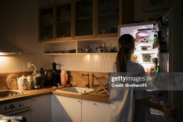 junge frau, die nachts im offenen kühlschrank nach essen sucht - open fridge stock-fotos und bilder