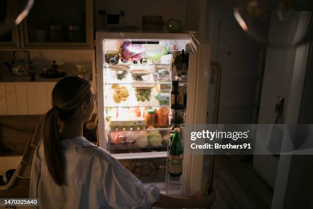 giovane donna che guarda in frigo di notte - aprire foto e immagini stock