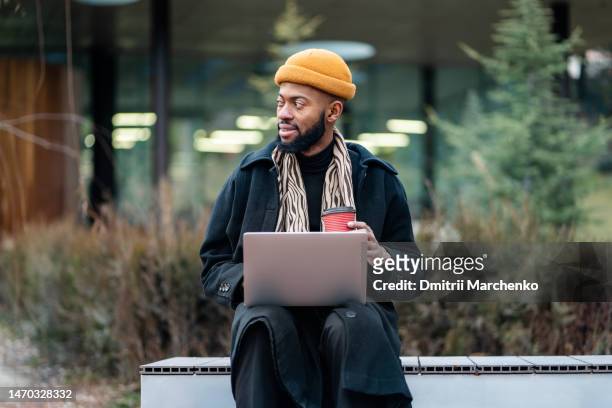 positive black man freelancer pondering new idea while sit on bench with paper cup coffee look side - georgian man stock pictures, royalty-free photos & images