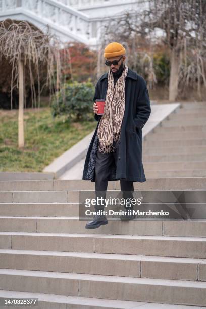 pensive hipster male in black long coat hold coffee with hand in pocket go down stairs walk outdoor - georgian man stock pictures, royalty-free photos & images