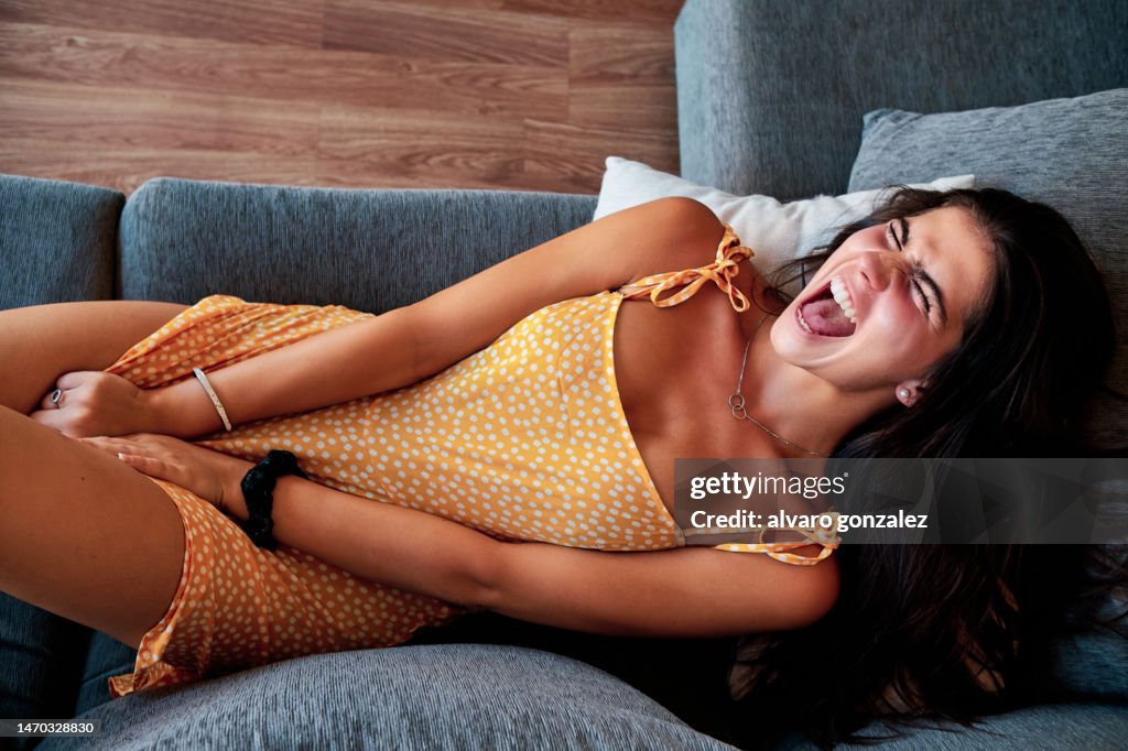 Woman suffering menstrual period pain lying on a sofa at home.