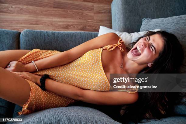 woman suffering menstrual period pain lying on a sofa at home. - cramp stock pictures, royalty-free photos & images