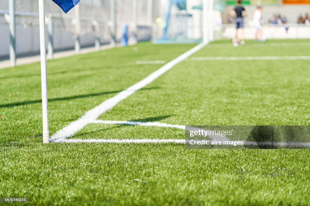 Side view of a soccer field:s flagpole and goal. Close up of a flag pole and a goal at the distance,